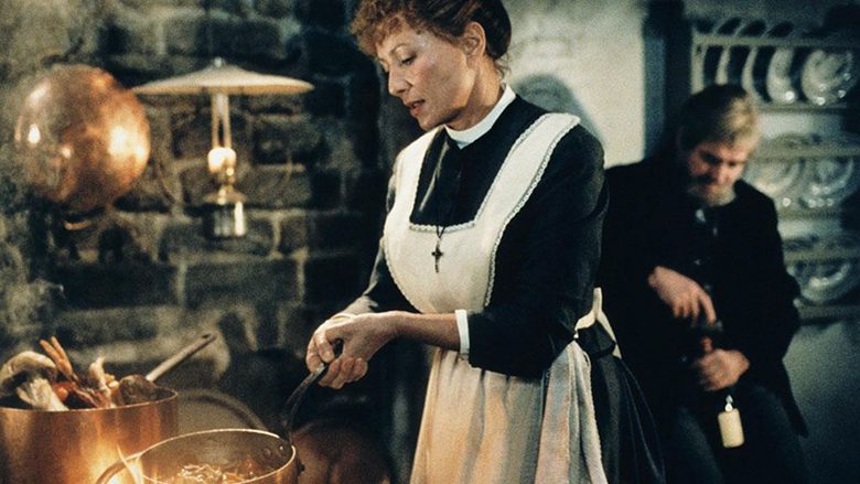 A Festa de Babette. Descrição da imagem: Freira cozinha enquanto homem abre uma garrafa de vinho ao fundo.