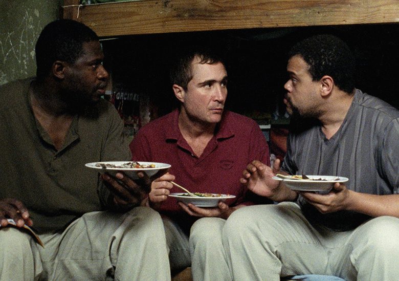 Estômago. Descrição da imagem: Três homens sentados em um beliche, comendo e se entreolhando com cara de assustados.