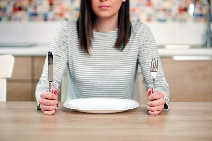 Erros alimentares: Ficar grandes intervalos sem se alimentar. Descrição da imagem: mulher com garfo, faca e prato vazio na frente dela.